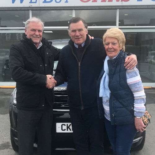 Angus MacKinnon in between two customers, smiling and shaking hands.